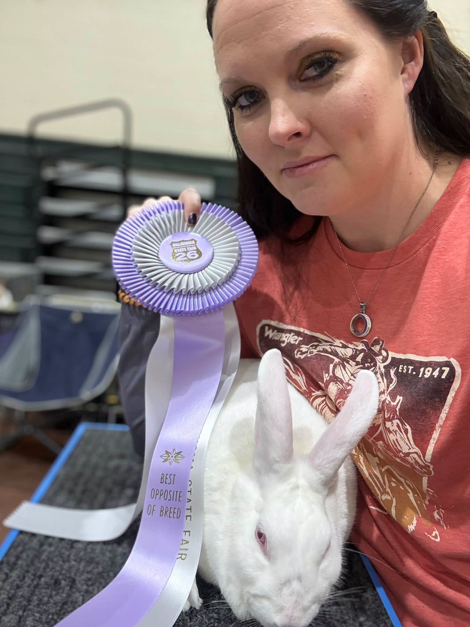 A person holding a lavender Best Opposite of Breed rosette next to a white rabbit